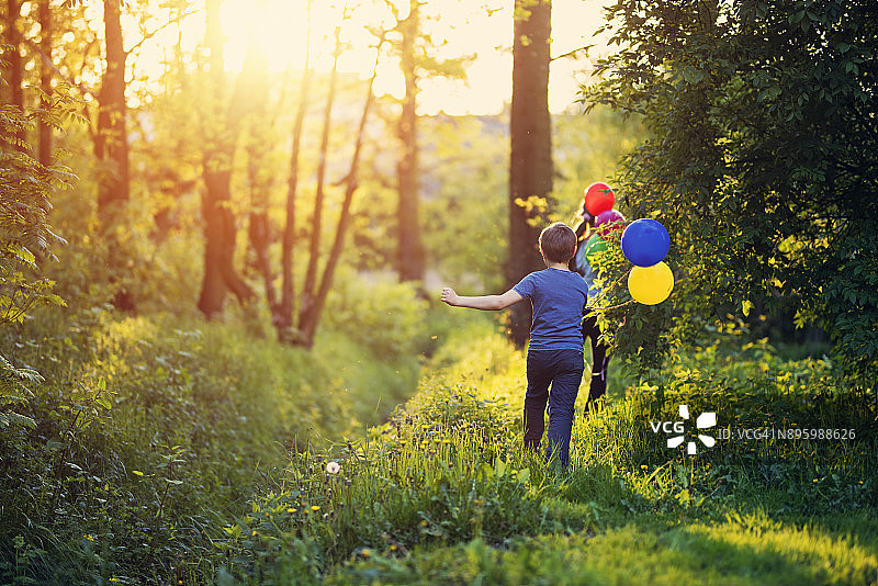快乐的孩子们拿着气球在春天的森林里奔跑图片素材