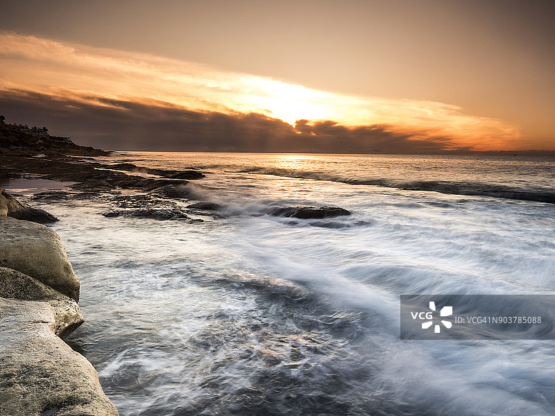 橙色太阳的出口，在海面上，在一个有岩石和波浪运动的海岸地带。西班牙瓦伦西亚社区阿利坎特。图片素材