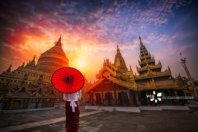 在缅甸蒲甘，一名身份不明的缅甸妇女拿着传统的红伞，看着金瑞zigon宝塔图片素材