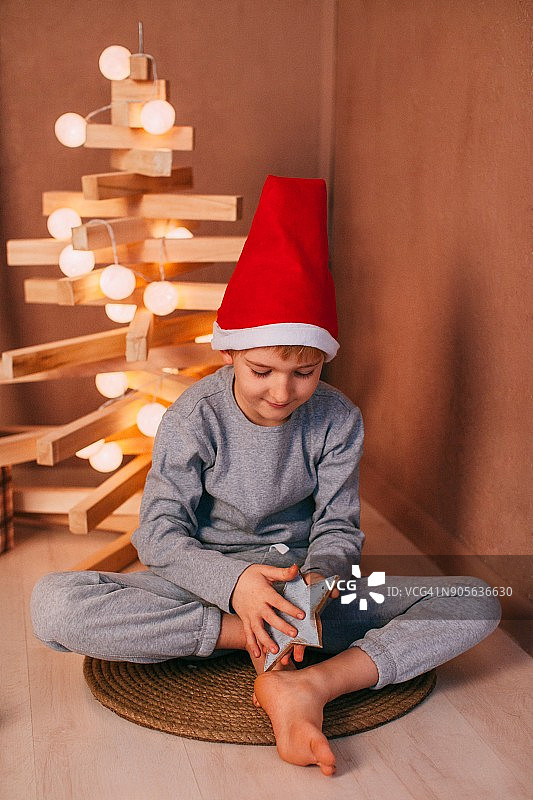 男孩坐在地板上，旁边是一棵现代圣诞树图片素材