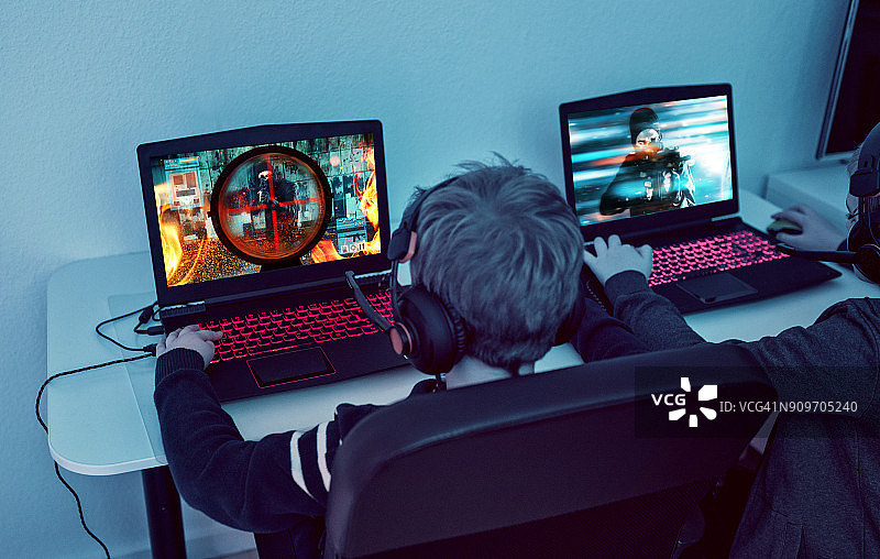 孩子们晚上在笔记本电脑上玩电子竞技游戏的后视图图片素材