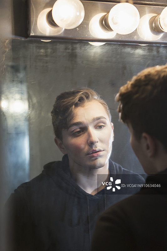 一个严肃的年轻人在更衣室里盯着镜子里的倒影图片素材