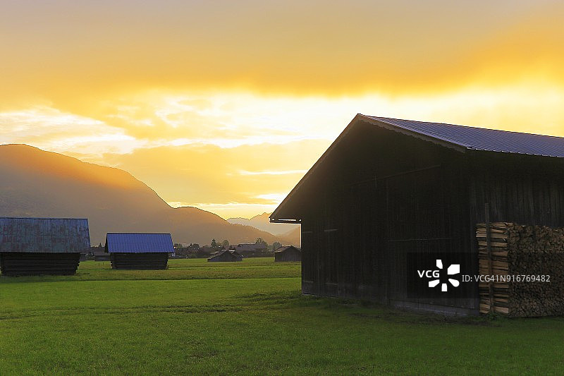 德国巴伐利亚的加尔米施，金色黎明的巴伐利亚阿尔卑斯山和木制谷仓图片素材