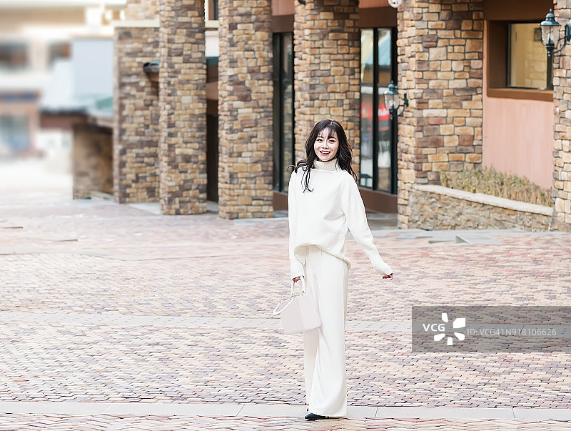 穿着白色高领毛衣和白色裤子在街上的时尚女性图片素材