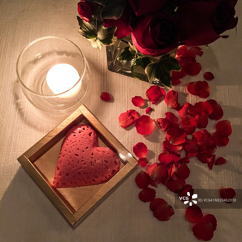 情人节的装饰有蜡烛、玫瑰、鲜花、玫瑰花瓣、草莓粉巧克力放在白色的桌子上图片素材