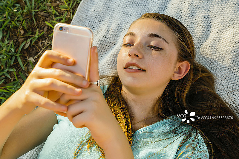 一个白人女孩躺在毯子上用手机发短信图片素材