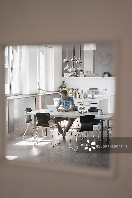 一个人坐在厨房的桌子旁用笔记本电脑工作图片素材