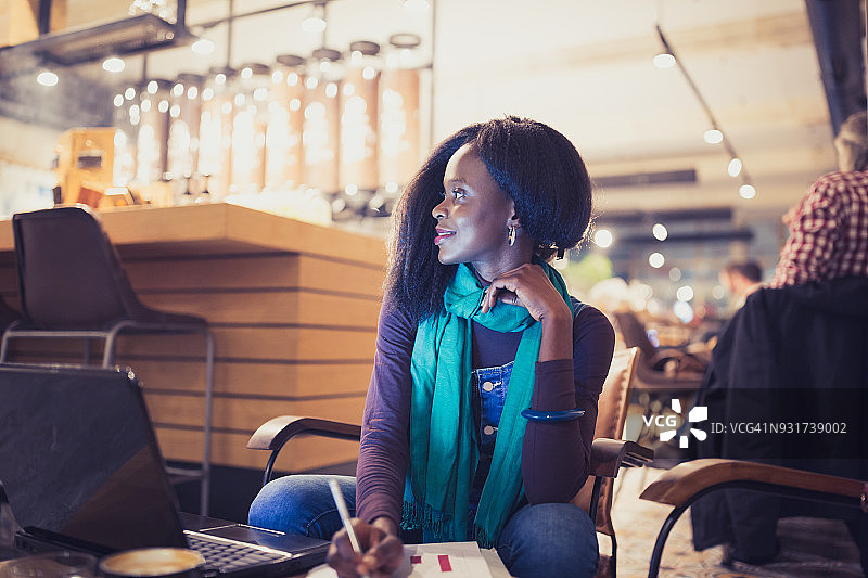 一位非洲裔美国年轻女性，在咖啡馆的咖啡休息时间，用笔记本电脑工作，浏览文档图片素材