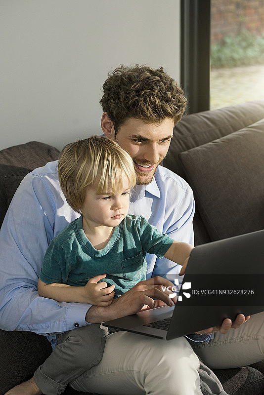 父亲和儿子看笔记本电脑在家里的沙发上图片素材