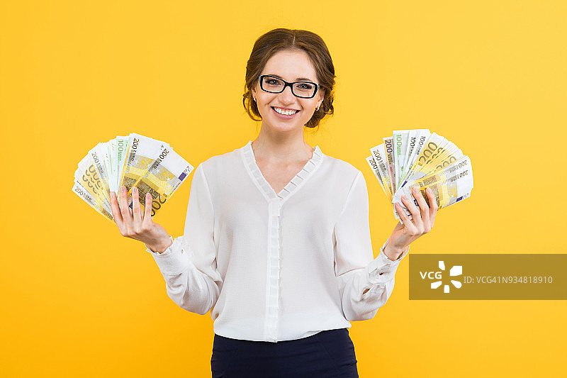 肖像自信美丽的年轻女商人与金钱在她的手中站在黄色的背景图片素材
