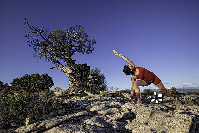 一位成年妇女在户外的岩石上练习瑜伽姿势图片素材