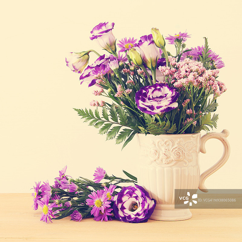 白色背景的木桌上，花瓶里放着一束夏日的紫色鲜花。图片素材