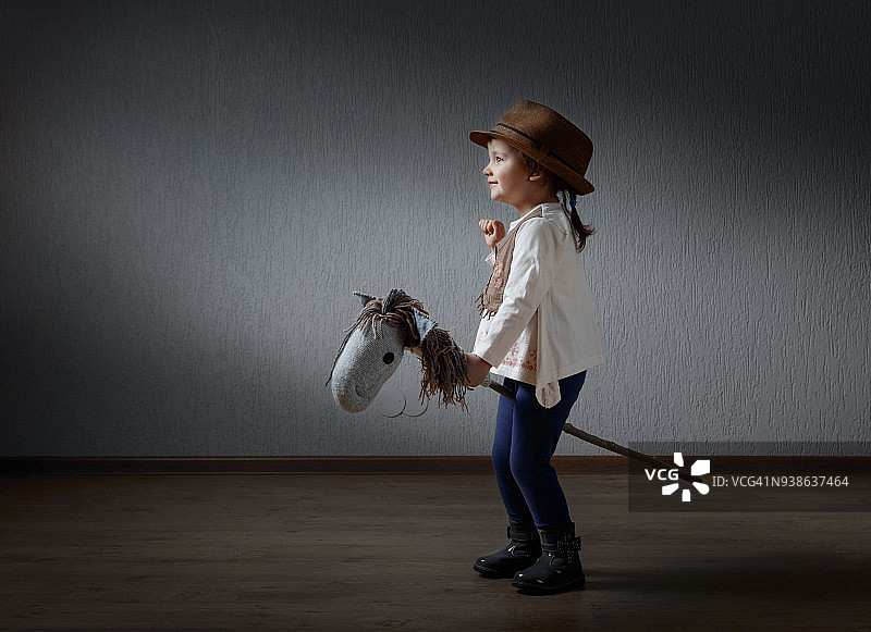可爱的小女孩打扮得像个牛仔在玩自制的马。图片素材