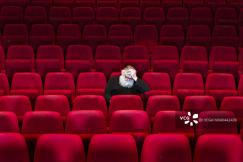 一个留着白胡子的男人坐在空荡荡的电影院，睡着了图片素材