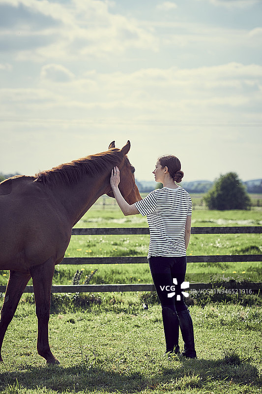 一个年轻女子和她的马站在围场里图片素材
