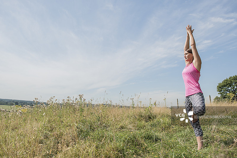 一个女人在外面的草地上享受阳光，同时练习瑜伽图片素材