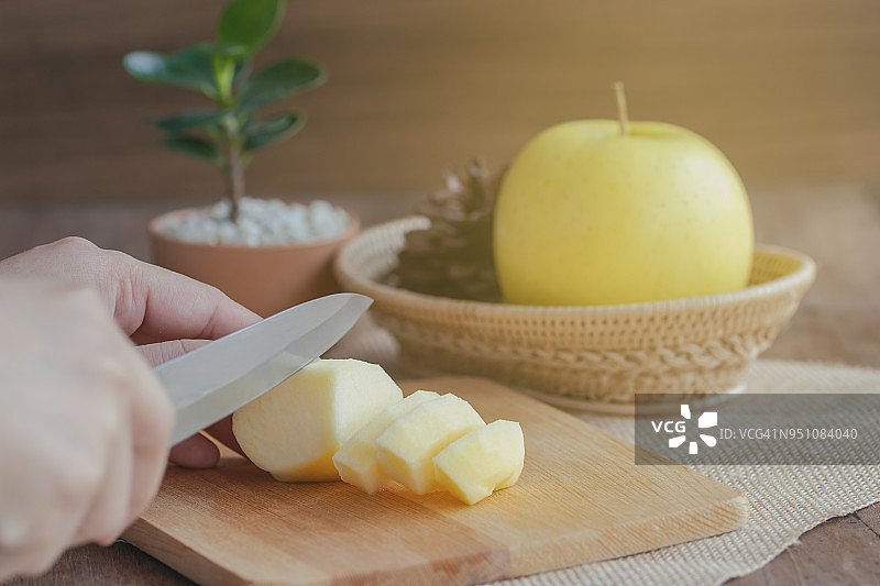 女人们在阳光下用刀把新鲜的Shinano金苹果切成小块，做成点心和沙拉，或者为家人准备自制的苹果派。家庭烹饪概念图片素材