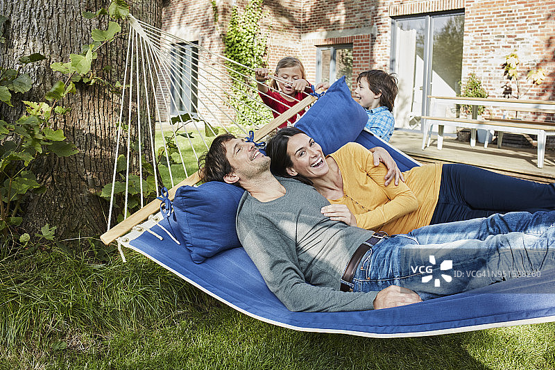 快乐的家庭在他们家花园的吊床上玩耍图片素材