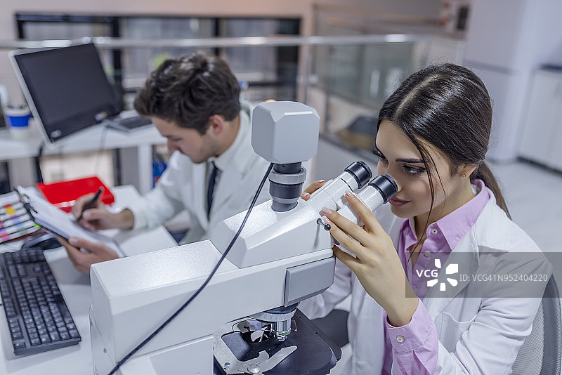 一位女科学家通过显微镜观察的侧视图图片素材