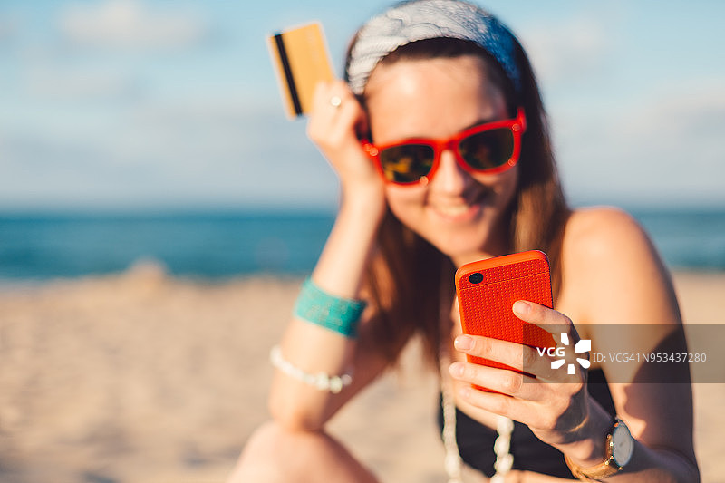 快乐的女孩在海滩度假网上购物与信用卡图片素材