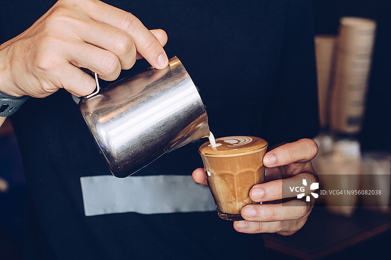 咖啡师制作卡布奇诺/拿铁时，将牛奶倒入咖啡杯，制作拿铁艺术。图片素材