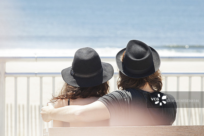 后视图的夫妇戴着帽子，而坐在沙滩长椅上图片素材