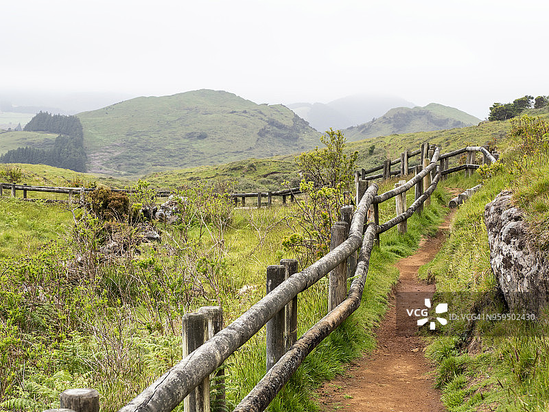 在葡萄牙亚速尔群岛的Terceira岛的田野上，有土路和绿色的草地，还有由树干做成的扶手。图片素材
