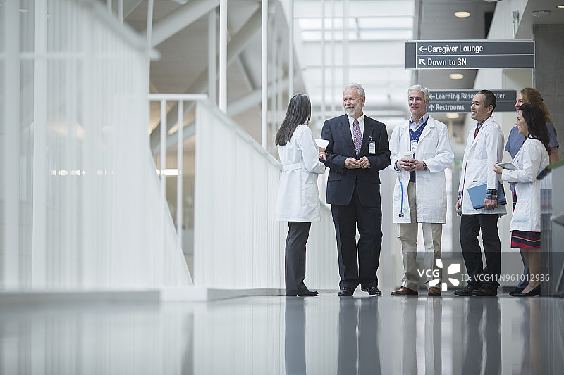 高级医生站在医院走廊上与同事讨论图片素材