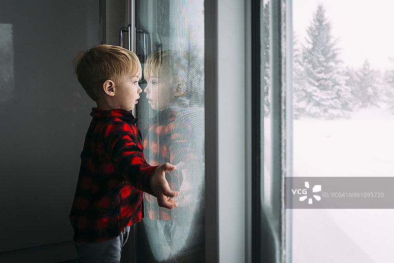 男孩在冬天站在家里从窗户往外看的侧视图图片素材