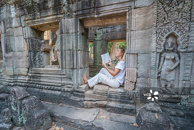 友好美丽的女性旅行者拿着旅游指南阅读关于柬埔寨吴哥窟建筑群的旅游信息图片素材