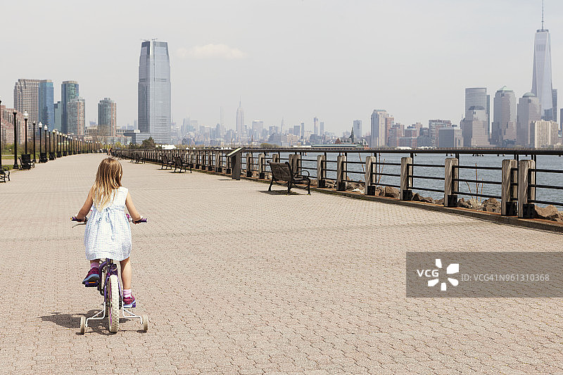 在城市天际线的背景下，女孩骑自行车散步的后视图图片素材