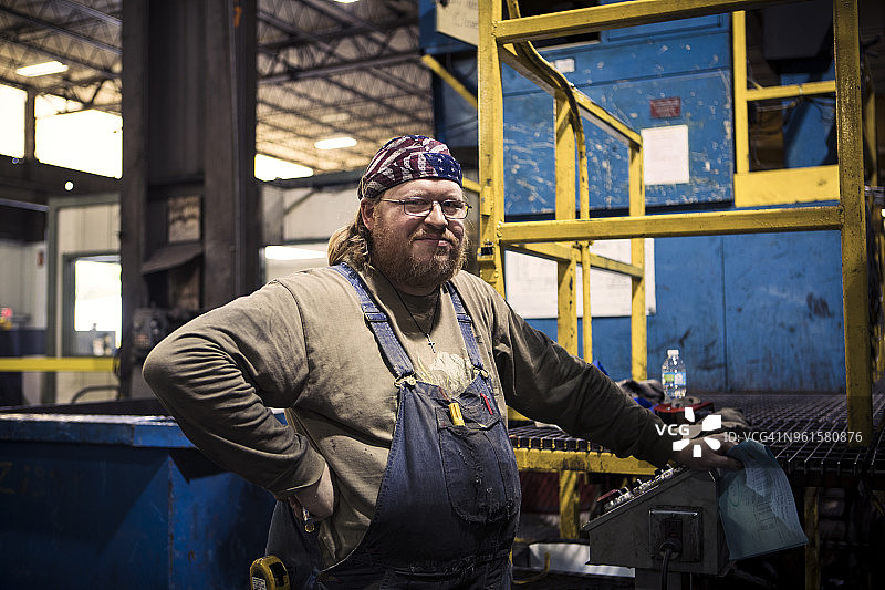 在金属工业中，手放在臀部的体力劳动者站在机器旁的肖像图片素材