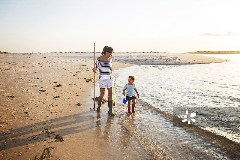 在阳光灿烂的日子里，母亲和女儿带着耙子在海边散步图片素材