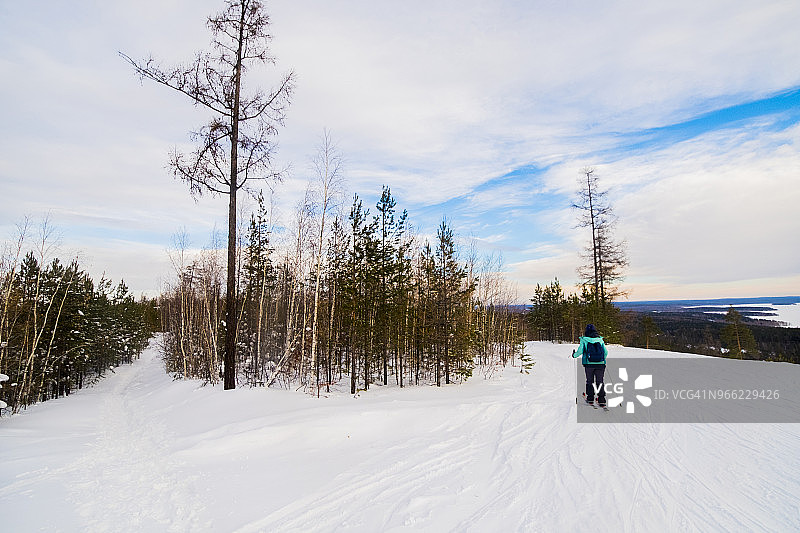 在多云的天空下，滑雪者在白雪覆盖的田野上滑雪的后视图图片素材