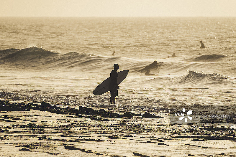 日落时分，一个人站在海面上，背着冲浪板图片素材