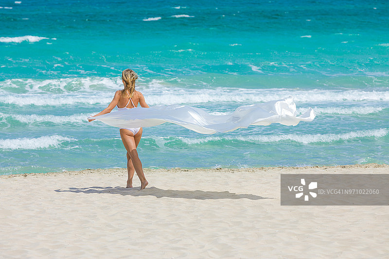 年轻女子在一个田园诗般的海滩上拿着白色的织物图片素材