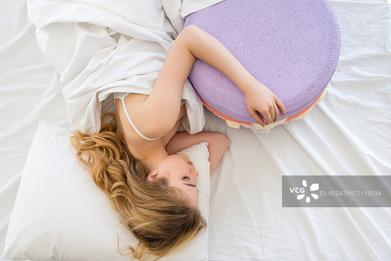 顶视图的金发女人睡在床上的大紫色马卡龙图片素材