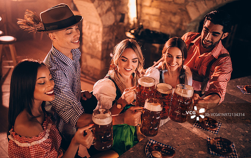 年轻的多民族朋友在慕尼黑啤酒节上用啤酒杯敬酒图片素材