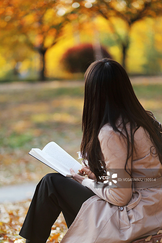 年轻女子与书在秋天的公园图片素材