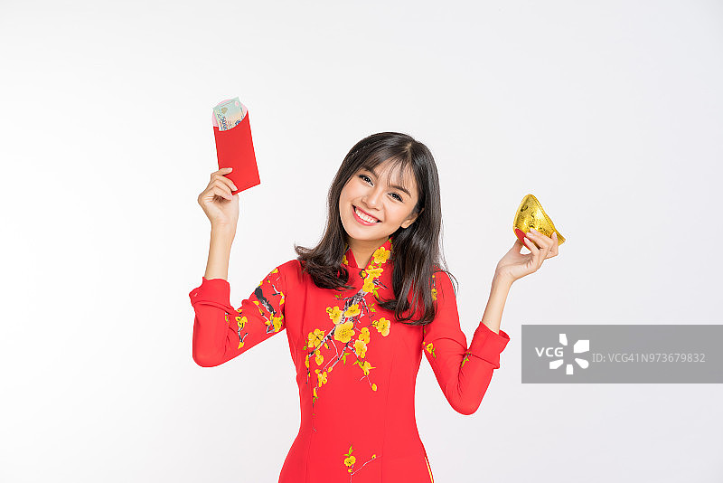 年轻女子穿着越南红色的敖戴，面带微笑，双手拿着一叠金元宝和新年红包图片素材