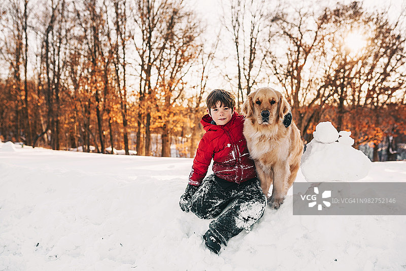 一个男孩和他的金毛猎犬坐在雪地里的肖像图片素材