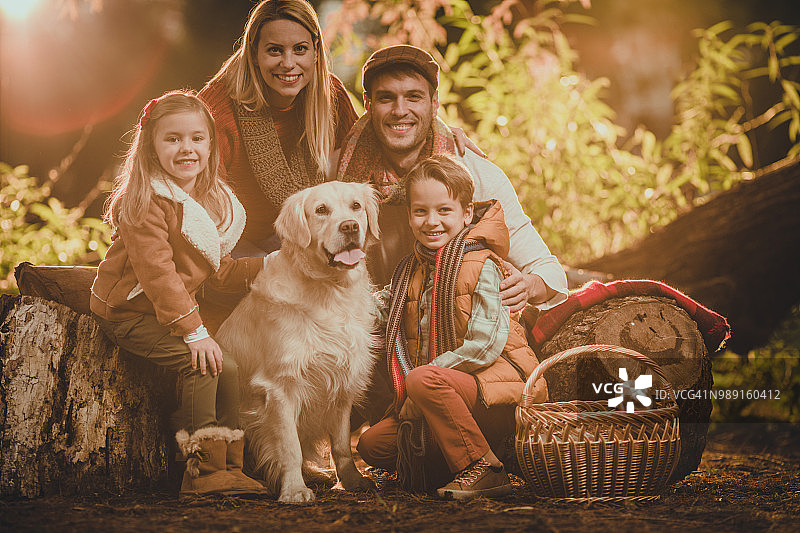 年轻幸福的家庭享受与他们的猎犬野餐在秋天的一天。图片素材