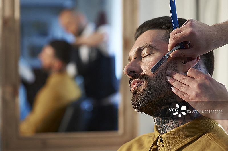 理发师用传统剃须刀为纹身的潮人刮胡须。图片素材