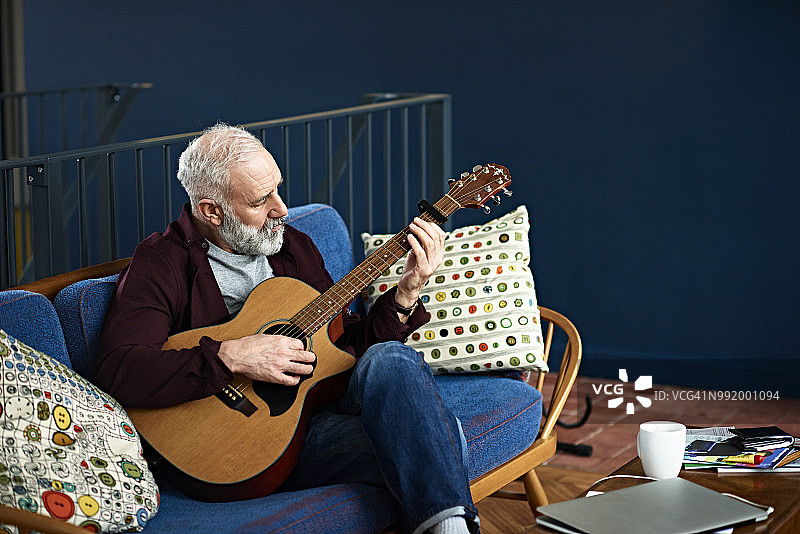 熟练的音乐家坐在沙发上弹奏古典吉他图片素材