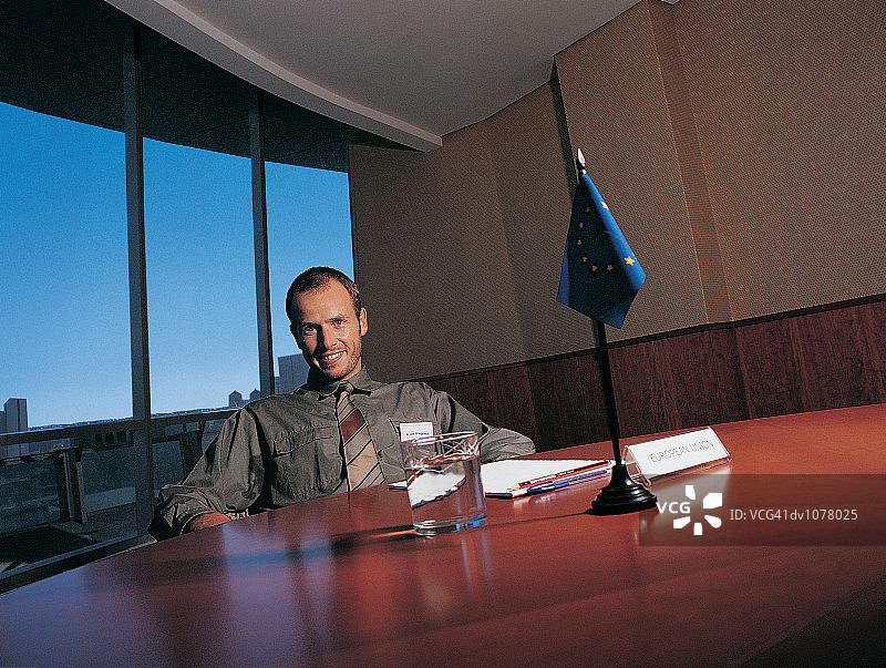 一个商人坐在欧盟旗帜旁的会议桌旁的肖像图片素材