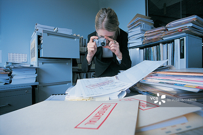 女商人在杂乱的办公室里拍摄机密文件图片素材