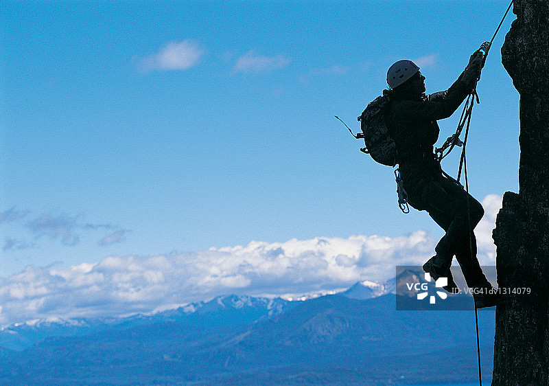 侧面剪影的一个登山者挂在岩石上的绳子图片素材