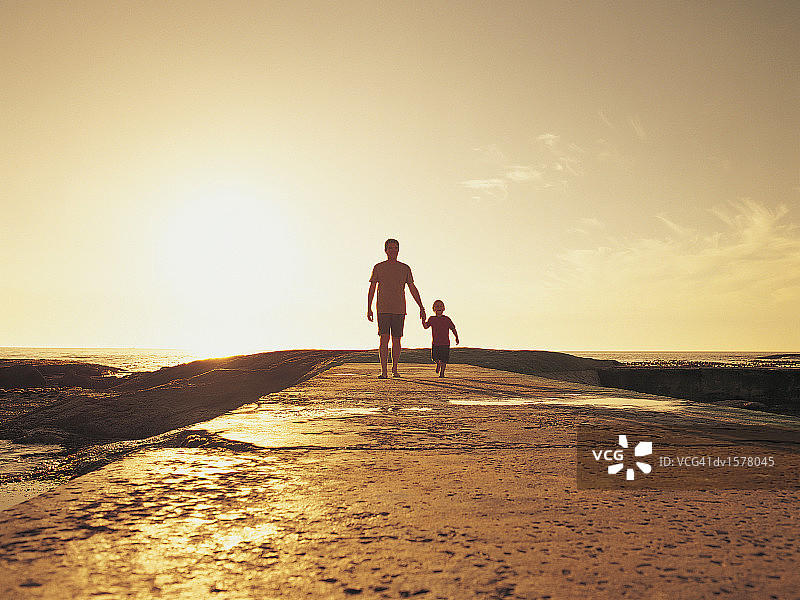 男孩和他的父亲在阳光下的海滩上散步图片素材