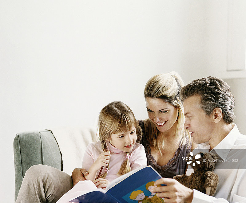 一对夫妇坐在沙发上给他们的小女儿读书图片素材
