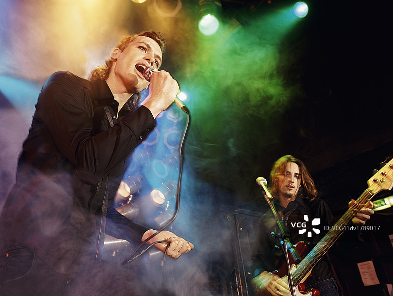 男歌手和吉他手在一个独立乐队表演在烟雾，聚光灯舞台图片素材